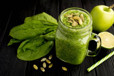 Siyah ahşap arka plan üzerinde ıspanak, elma ve kabak çekirdeği ile Yeşil smoothies
