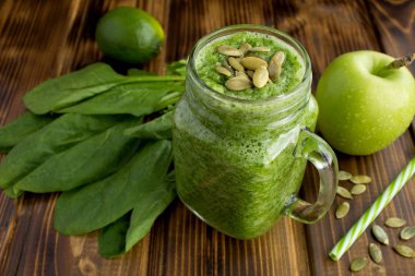 Kahverengi ahşap arka plan üzerinde ıspanak, elma ve kabak çekirdeği ile Yeşil smoothies