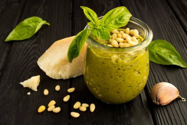Cam kavanozda sos pesto ve siyah ahşap arka plan üzerinde malzemeler