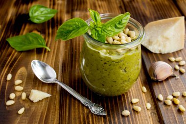 Cam kavanozda sos pesto ve kahverengi ahşap arka plan üzerinde malzemeler