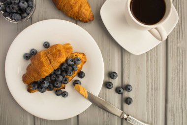 Kahvaltı: kahve, fıstık ezmesi ile kruvasan ve gri ahşap arka plan üzerinde yaban mersini. Üst te. Kopyalama alanı.