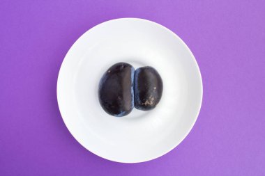 Ugly food. Ugly blue plum on a white plate in the center of the purple background. Top view. clipart