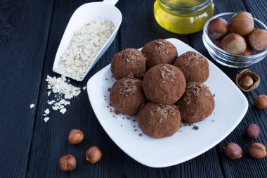 Siyah ahşap arka plan üzerinde beyaz plaka üzerinde fındık, kakao, yulaf tahıl ve bal ile enerji topları