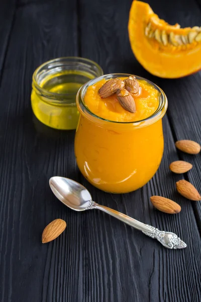 Siyah ahşap arka plan üzerinde cam kavanozda kabak, badem ve bal ile püre. Kopya alanı. Konum dikey.