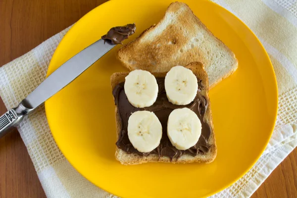 Bread with chocolate cream and banana on the yellow plate