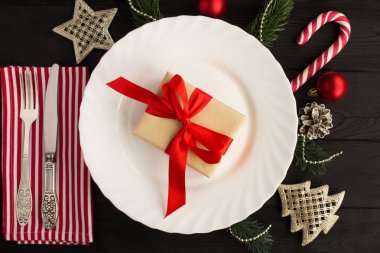 Siyah ahşap arka plan üzerinde hediye ve Noel kompozisyon ile beyaz plaka. Üst te. Kopyalama alanı.