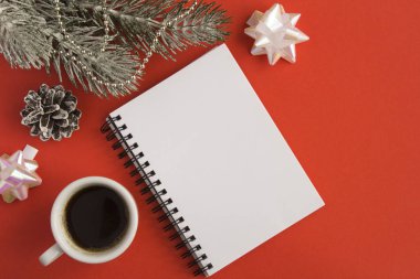 Açık not defteri, beyaz fincanda sade kahve ve kırmızı arka planda Noel kompozisyonu. Uzayı kopyala Üst görünüm.