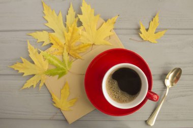 Kırmızı seramik fincanda koyu kahve, gri ahşap arka planda sarı yapraklar. Üst Manzara. Sonbahar bileşimi.