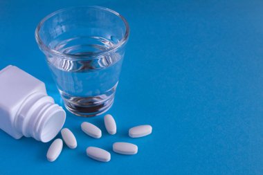 Beyaz haplar ve mavi arka planda bir bardak su.