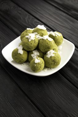 Enerji topları kibrit tozu, fıstık, hurma ve hindistan cevizi cipsi ile siyah ahşap arka planda beyaz tabakta. Konum dikey.