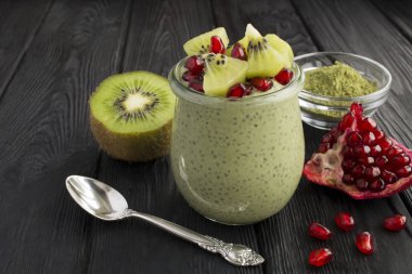 Siyah ahşap arka plandaki cam kavanozda chia, kivi ve nar tohumlu puding. Yakın çekim..