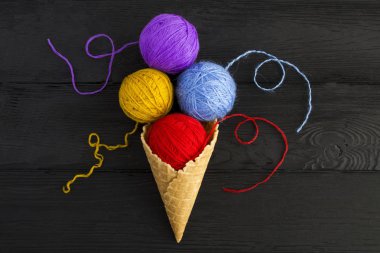 Siyah ahşap arka planda örgü örmek için renkli iplikleri olan dondurma külahı. Üst Manzara. Boşluğu kopyala.