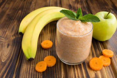 Kahverengi ahşap arka planda muz, elma ve havuçlu meyve püresi. Yakın çekim..