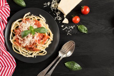 Domates soslu İtalyan makarnası ve koyu ahşap arka planda siyah tabakta parmesan. Üst Manzara. Boşluğu kopyala.