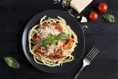Domates soslu İtalyan makarnası ve koyu ahşap arka planda siyah tabakta parmesan. Üst görünüm.