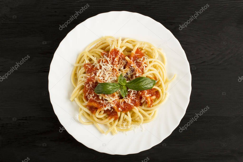 Italian pasta with tomato sauce and parmesan in the white plate in the center of  the black wooden background. Top view.