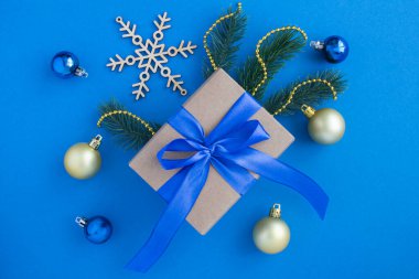 Mavi fiyonklu bir hediye ve mavi arka planda noel kompozisyonu. Üst Manzara. Boşluğu kopyala.