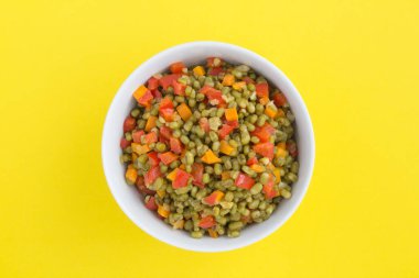 Sarı arka plandaki beyaz kasede sebzeli Mung fasulyesi. Üst Manzara. Yakın çekim..