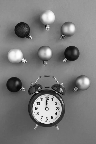 Top view of the black  alarm clock, black and grey Christmas balls in the center of the grey surface