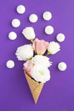 Pembe ve beyaz çiçekli dondurma külahı ve menekşe arka planında beyaz krema.