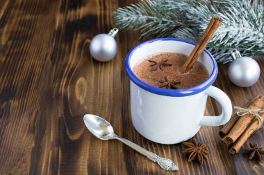 Beyaz metal bardakta tarçın ve ahşap arka planda Noel kompozisyonu olan sıcak kakao.