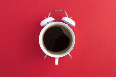 Kahvenin üst görüntüsü kırmızı arkaplanın ortasındaki beyaz çalar saatin kadranında.