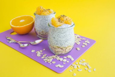Şili soslu puding, yulaf ezmesi ve turuncu menekşe kesim tahtasındaki cam kavanozlarda sarı arka planda.