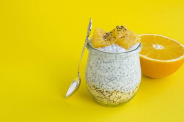 Sarı arka plandaki cam kavanozda puding, yulaf ezmesi ve portakal.