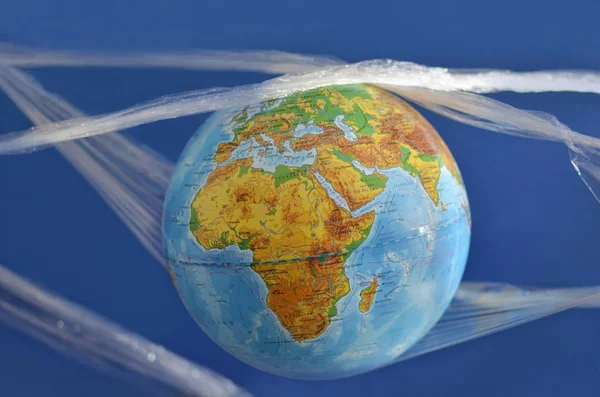 The earth is suspended in a plastic plastic disposable packaging, on a blue background. The concept of environmental pollution by polyethylene plastic waste, environmental problems.