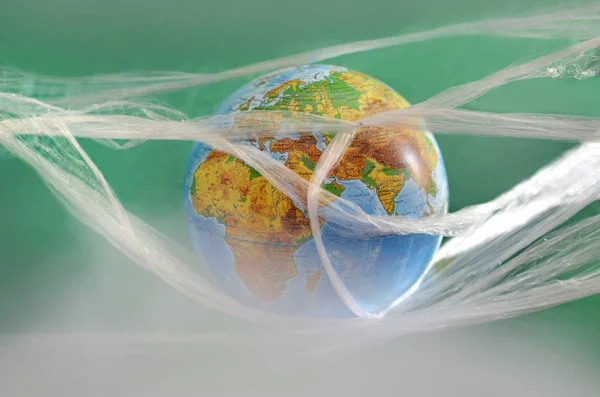 The earth is suspended in a plastic plastic disposable packaging, on a green background. The concept of environmental pollution by polyethylene plastic waste, environmental problems.