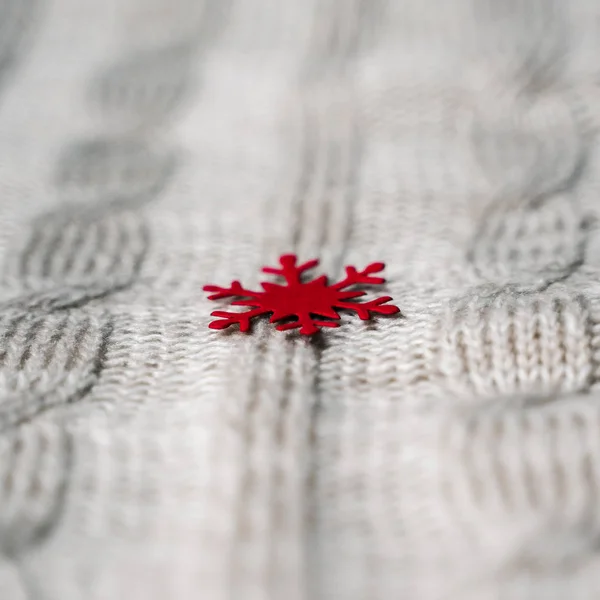Beautiful light gray knitted pattern with red paper snowflake , knitted scarf close up. Knitted background, square