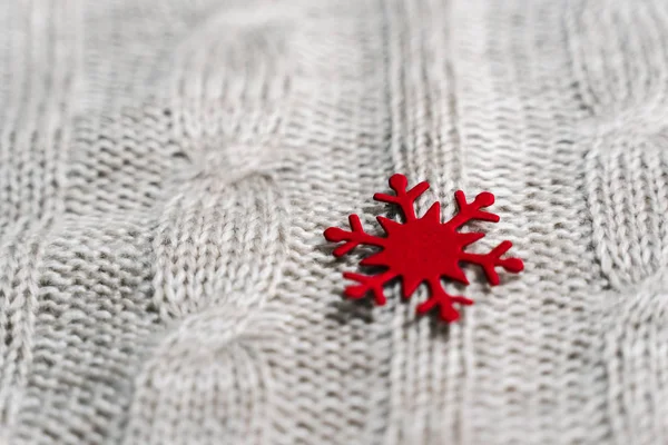 Beautiful light gray knitted pattern with red paper snowflake , knitted scarf close up. Knitted background.