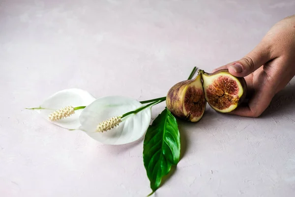 Mão segurando um todo fresco e cortar figos com algumas flores em um fundo de mármore rosa claro, espaço de cópia. Foco selecionado — Fotografia de Stock