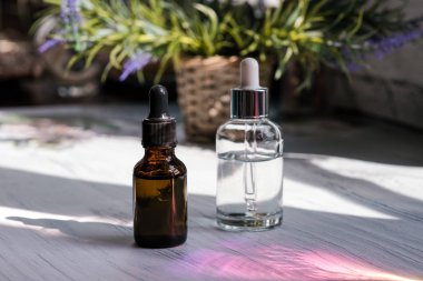 Kahverengi, damlalıklı berrak gözlükler, koyu arka planda organik yeşil yapraklar. Bitkisel ekstresi ile serum veya uçucu yağ