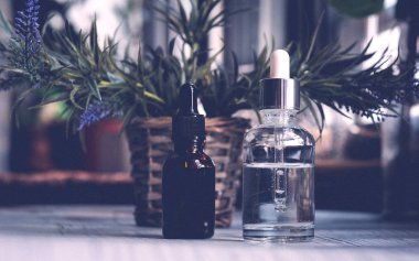 Kahverengi, damlalıklı berrak gözlükler, koyu arka planda organik yeşil yapraklar. Bitkisel ekstresi ile serum veya uçucu yağ