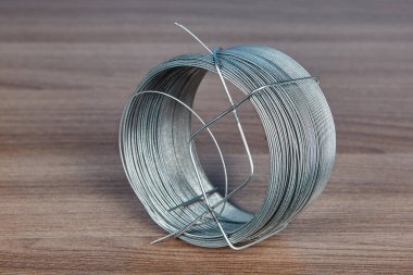 Küçük çaplı çelik tel bir rulo üzerinde ahşap masa üstü yatıyor.