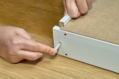Mobilya montaj, carpenter'ın parmakları bir plastik dübel PIN sunta deliğe çekmece yakın çekim montaj eklemek.