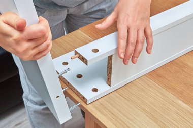 A furniture assembler connects parts of the table with help of wooden dowel pin and connector bolts. clipart
