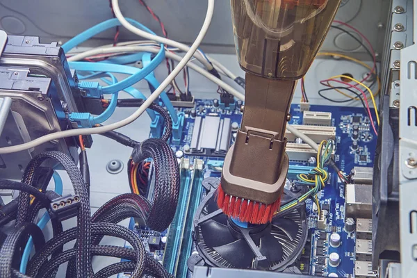 Fan of central processing unit and motherboard inside personal computer are cleaning by upright vacuum cleaner.