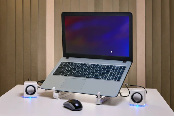 An runned notebook on a cooling rack and two small white USB speakers with an blue LED lights.