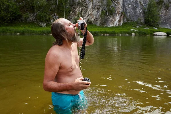 Marure muž stojí ve vodě s fotoaparátem. — Stock fotografie