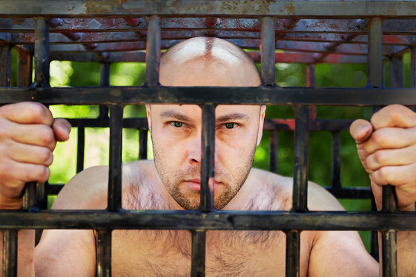 One man is looking from behind a prison cell.