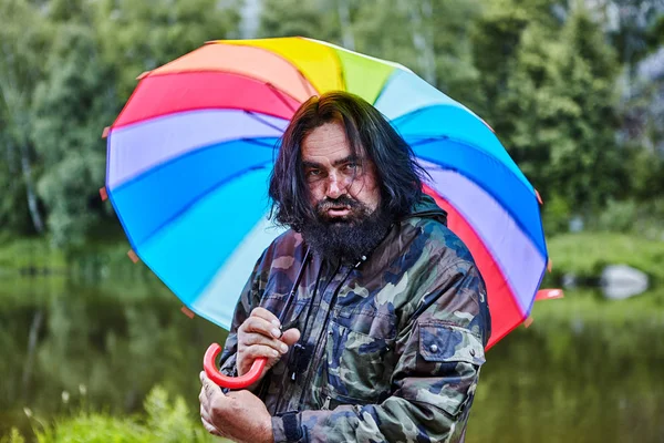 Reifer, zotteliger Mann unter Regenbogenschirm. — Stockfoto