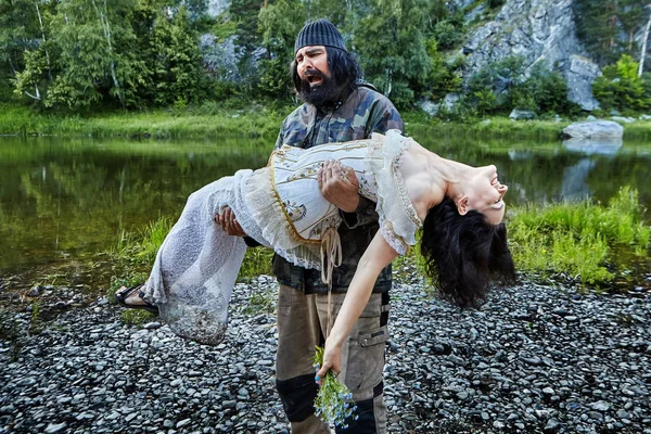 Brutal man with a woman in her arms. — Stock Photo, Image