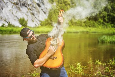 Bir genç adam doğada akustik gitar çalar.