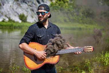 Genç bir adam sigara içen bir gitar tutar.