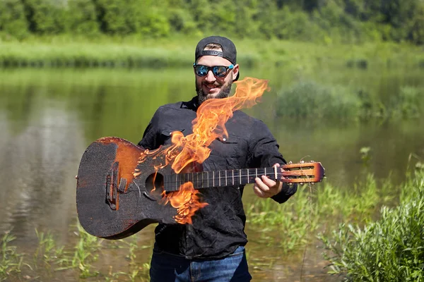 Ein Gitarrist zündete seine Gitarre in der Nähe eines Flusses an. — Stockfoto