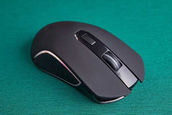 Wireless gaming computer mouse in black, with led light on green background. Battery powered input device to control the cursor on the PC screen.