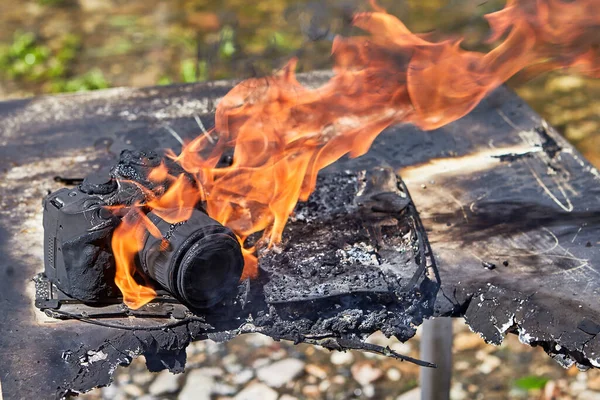 Forest fire spread to campground, property of tourists burned, including photo equipment. The digital SLR camera is destroyed by a flame, it is burnt, melted and charred. Gadget is damaged by flame.