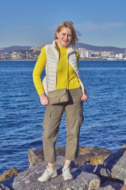 Genç beyaz bir kadın Marmara Denizi 'nin arka planında ve karşı kıyıdaki İstanbul şehrinin karşısında duruyor. Büyükada Adası, Türkiye 'deki Prenslerin Adalarından biri, güneşli kış günü.
